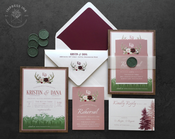 Rustic Antler Mountain Invitation with landscape mountain silhouette in shades of green, floral antler monogram, and pink accents
