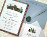 Rustic Watercolor Barn Invitation with a dark brown barn surrounded by evergreen trees, wood backing layer and dusty blue envelopes.