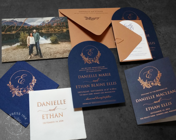 Navy Copper Arch Invitation with floral wreath monogram in copper foil on matte navy cardstock, terracotta colored envelopes